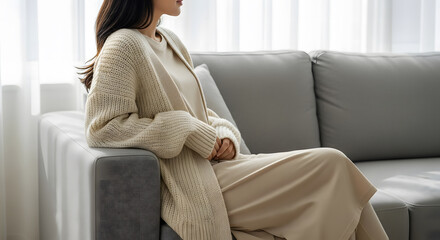 Woman in beige knit cardigan sitting on modern sofa armrest by w