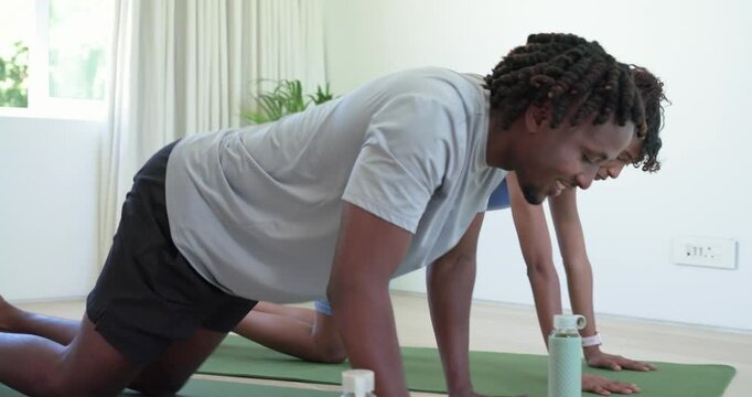 Couple high-fiving starting workout kneeling at home on green mats lowering into pushup pressing
