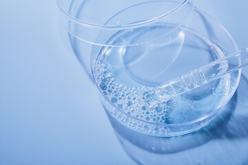 Petri dish holding blue liquid and pipette creating bubbles for cosmetic research