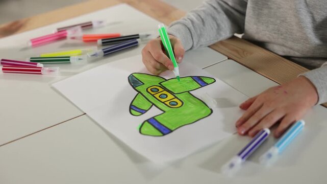 Little boy drawing plane with felt tip pen at wooden table indoors, closeup