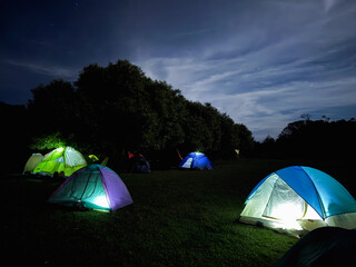 Long exposure photograph of a group of illuminated tents under a spectacular night sky in a forest clearing - Camping adventure concept
