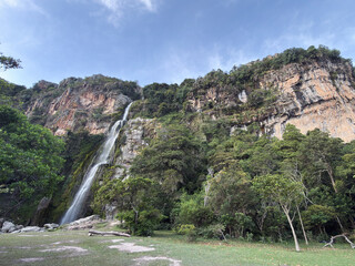 Majestic waterfall cascading down a steep rocky cliff surrounded by lush green forest under a blue sky - Wine Waterfall, Lara, Venezuela