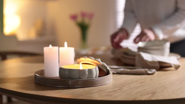 Beautiful burning candles and woman setting table at home, selective focus