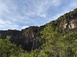  Picturesque waterfall cascading down a high rocky cliff in a lush tropical forest under a blue sky