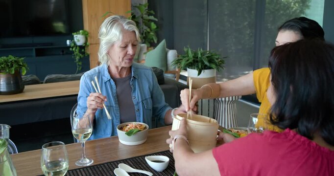 Diverse women sharing meal home, senior, woman in red reaching, serving dimsum from bamboo steamer