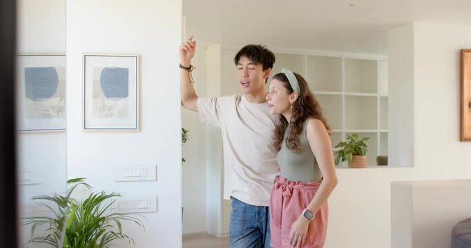 Diverse couple touring new flat after receiving keys, man pointing, woman laughing and leaning