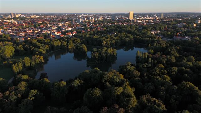 Air view over Kleinhesseloher See, artificial lake in the English Garden, Munich, Bavaria. Surrounded by trees, meadows, beer gardens and cultural landmarks. German urban nature site