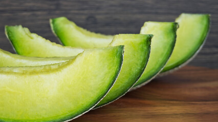 close up of a green cantaloupe slice on a piece of wooden.
