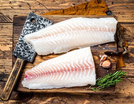 Fresh Raw cod loin fillet steaks on wooden board with butcher knife. wooden backgroun 