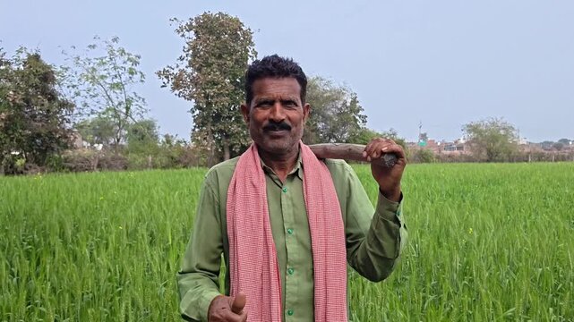 Confident Indian farmer carrying a traditional hoe and showing thumbs up in the field