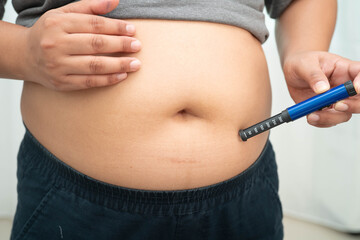 Asian woman injecting herself diabetes injecting insulin in stomach at home.