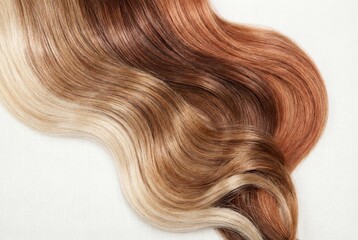 Fototapeta premium Shiny wavy hair strands with ombre gradient from blonde to copper red on white fabric background
