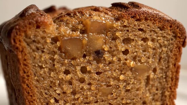 Extreme macro close-up of a slice of moist, sticky baked quick bread or cake loaf, featuring a dense, porous crumb texture and chunks of caramelized fruit filling.