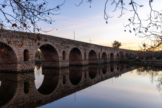 Romantic twilight photograph of the ancient Puente Romano arched roman bridge over the Guadiana River in Merida Spain (ESP) with vibrant sunset reflections
