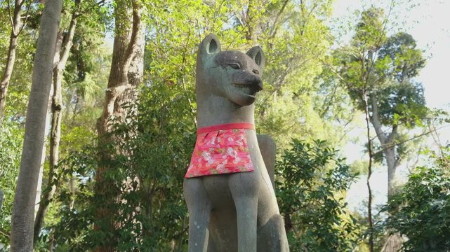 A fox statue with red scarves in the spiritual path of Fushimi Inari Taisha in Kyoto, Japan.