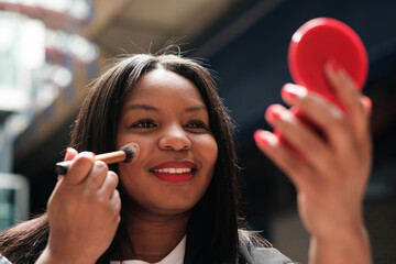 Businesswoman applying makeup with brush and mirror in urban setting