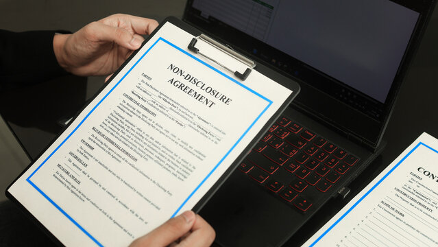 Serious business person hands holding non disclosure agreement paper clipboard near computer laptop with focused feeling about secret contract