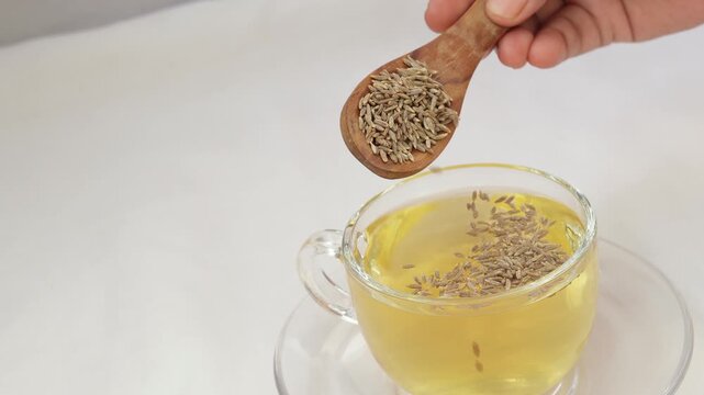 Herbal detoxifying drink isolated on white, i.e., Jeera water with some raw organic cumin in a wooden spoon.