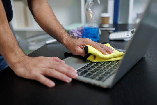 A man is cleaning a laptop with a yellow cloth. Concept of taking care of one's belongings and maintaining them in good condition. Scene is practical and focused on the task at hand
