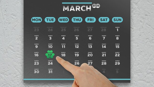 Close-up of a male hand pointing finger at the date of St. Patrick's Day 2026 on a black wall calendar
