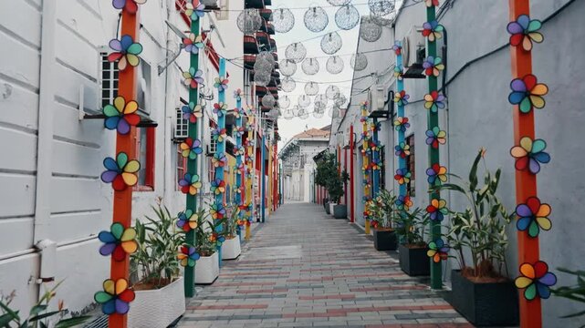 A narrow heritage alleyway is beautifully decorated with vertical rows of vibrant flower pinwheels and hanging lantern globes.