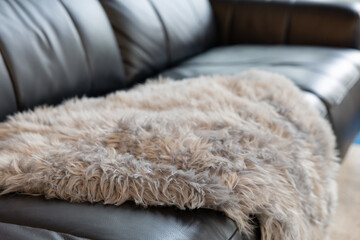 A black leather couch with a grey and white wool blanket on top of it. The blanket is made of fur and has a fuzzy texture.