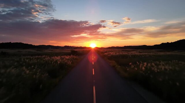 A long straight road stretches into the distance towards a vibrant sunset over