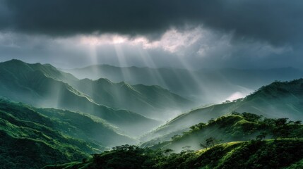 Sunlight pierces through dark clouds, illuminating rolling green mountain ridges and valleys