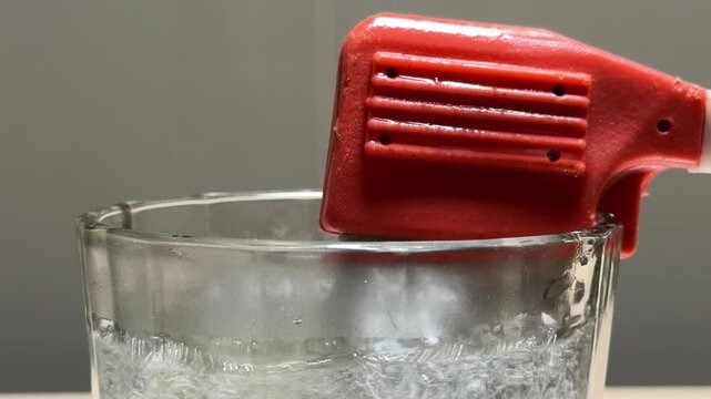 A red portable immersion heater rapidly boils water inside a glass cup. The intense heat generates a violent churning of large bubbles, resulting in a loud, roaring rumble and high-pitched splashing.