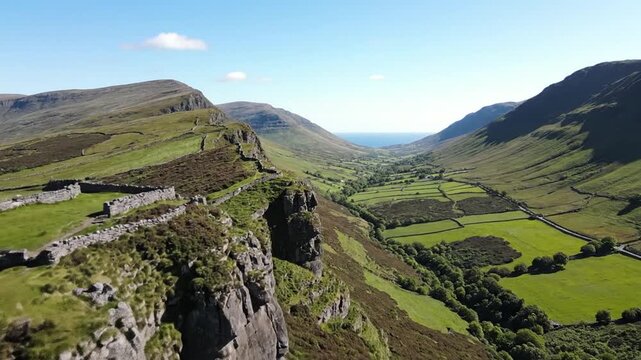 A stunning aerial view of a vibrant green valley, with mountains and stone walls under a clear blue sky