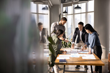 Four diverse business analysts discussing paper reports at meeting table, analyzing statistic research results, working together in business plan for project growth. Candid shot with copy space © fizkes