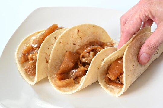 Hand holding a traditional plain pork skin taco (taco de cueritos "sin nada"), ready to eat on corn tortillas.