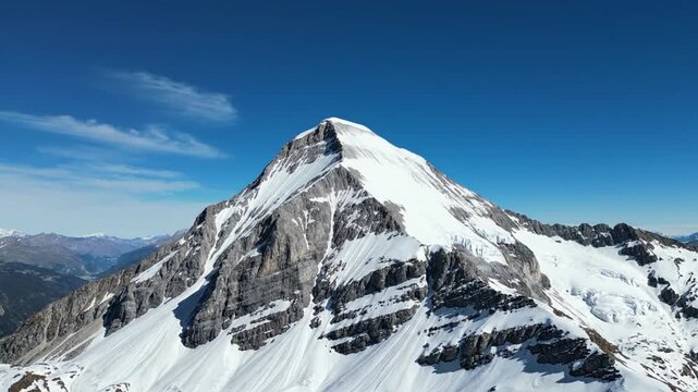 A high-angle view captures a majestic snow-capped mountain against a clear, deep blue sky