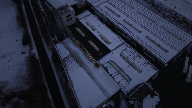 Aerial view of snow-covered factory roof in United States, showing industrial buildings, loading areas and winter conditions from above during cold seasonal weather. Flyover top down.