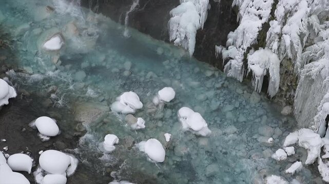 Aerial Stationary View of Frozen Shirahige Waterfall and Cobalt Blue Biei River in Winter, Hokkaido Japan