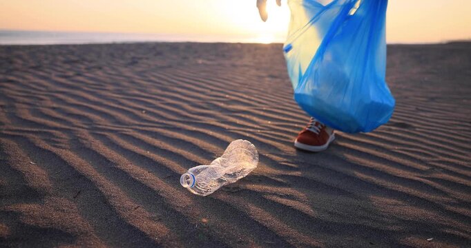 Young eco-friendly woman collect plastic bottles on a sandy beach. Girl volunteer clean up the environment during summer vacation. The concept of ecology and Earth day. Slow motion