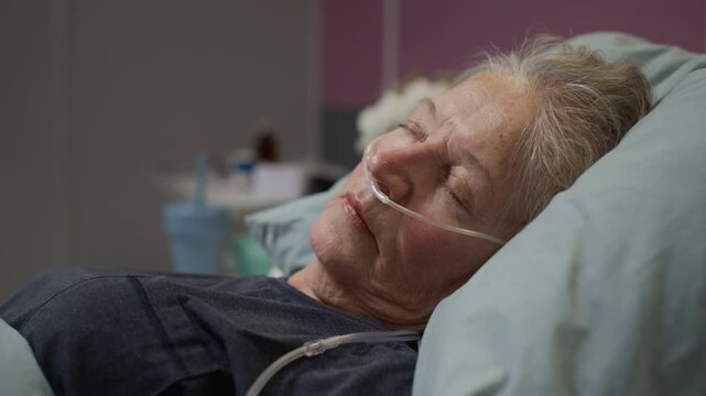 Rack focus close up shot of mature Caucasian female patient waking up in hospital bed while receiving oxygen treatment through nasal cannula