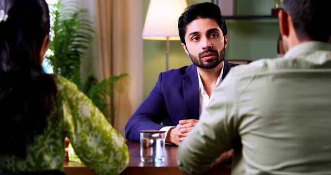 Indian couple visiting discussing with officer or executive shaking hands sitting across table after successful financial consultation and investment deal closure in modern corporate office interior