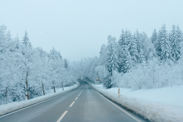 Obraz premium Winding winter highway through a deep snow-covered forest seen from a driver's point of view