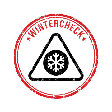 distressed circular red rubber stamp icon with grunge texture, featuring "wintercheck" text and a warning triangle snowflake symbol, isolated on bright white. concept of vehicle winter safety check