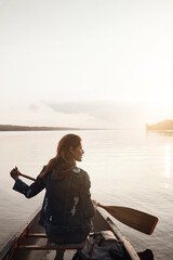 Fototapeta premium Canoe, reflection and woman on lake for travel, explore and adventure with back view in nature. Boat, think and person with paddle for summer vacation, holiday or sunshine with mockup space by water