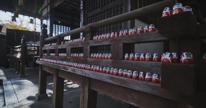 Long rows of tiny daruma dolls on wooden rails of ancient Japanese shrine - steady cam shot