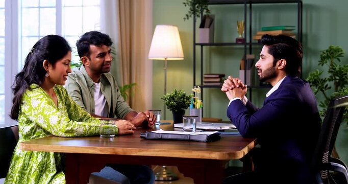 Indian couple visiting discussing with officer or executive shaking hands sitting across table after successful financial consultation and investment deal closure in modern corporate office interior
