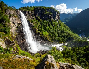 Obraz premium A majestic waterfall cascades down a rocky cliffside surrounded by lush greenery and mountains under a blue sky
