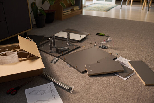 Flat pack furniture components lying on carpet with instruction manual, screws, tools and packaging scattered around, assembly process in progress in modern home interior