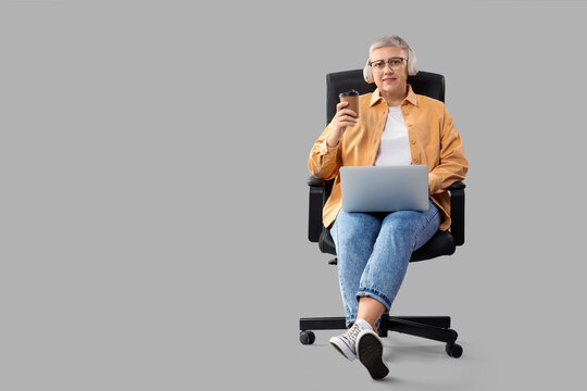 Female programmer with coffee and laptop in chair on light background