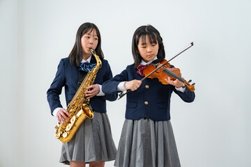 Fototapeta premium サックスとバイオリンを演奏する制服姿の女子生徒二人