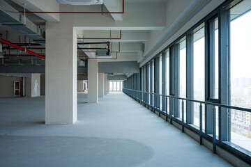 Unfinished office building corridor with exposed pipelines and floor-to-ceiling windows