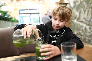 Boy pouring green juice into glass at cafe