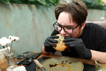Man in glasses eating hamburger with black gloves
